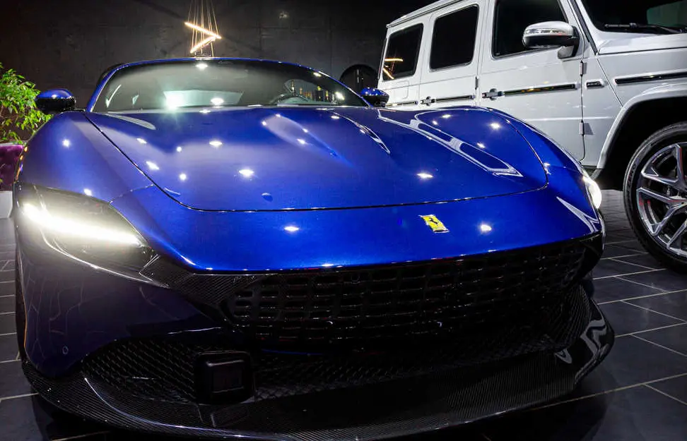 Blue Ferrari from the front, a white Mercedes G-Class in the background