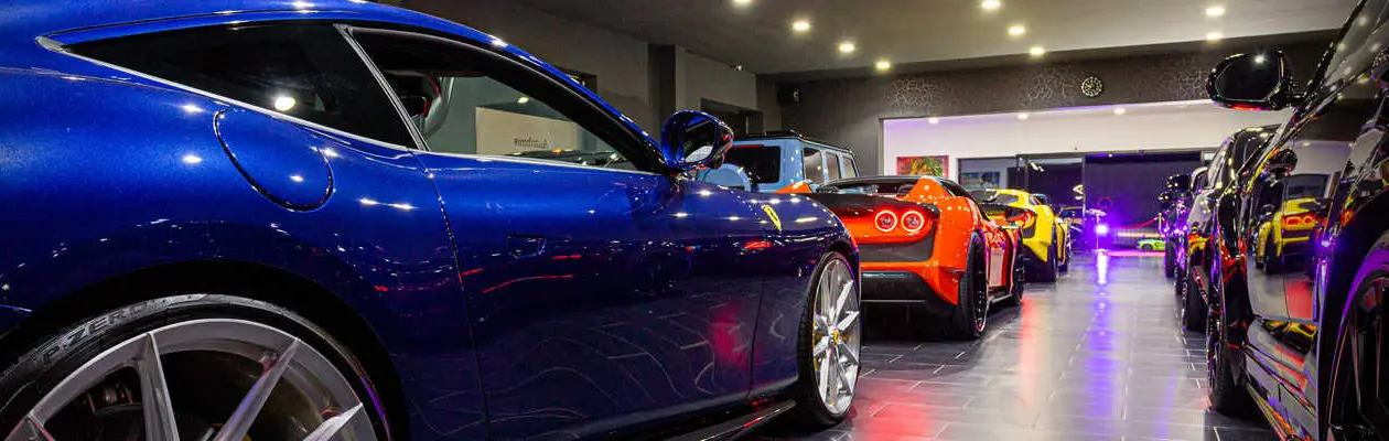 Blue Ferrari in the foreground, the vehicle lineup behind it under purple hall lighting
