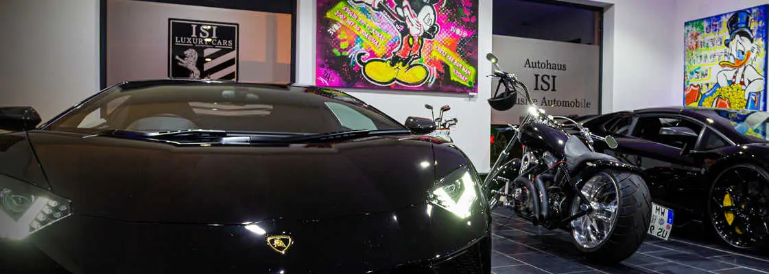 Dark sports car next to a custom motorcycle, the ISI wall crest in the background